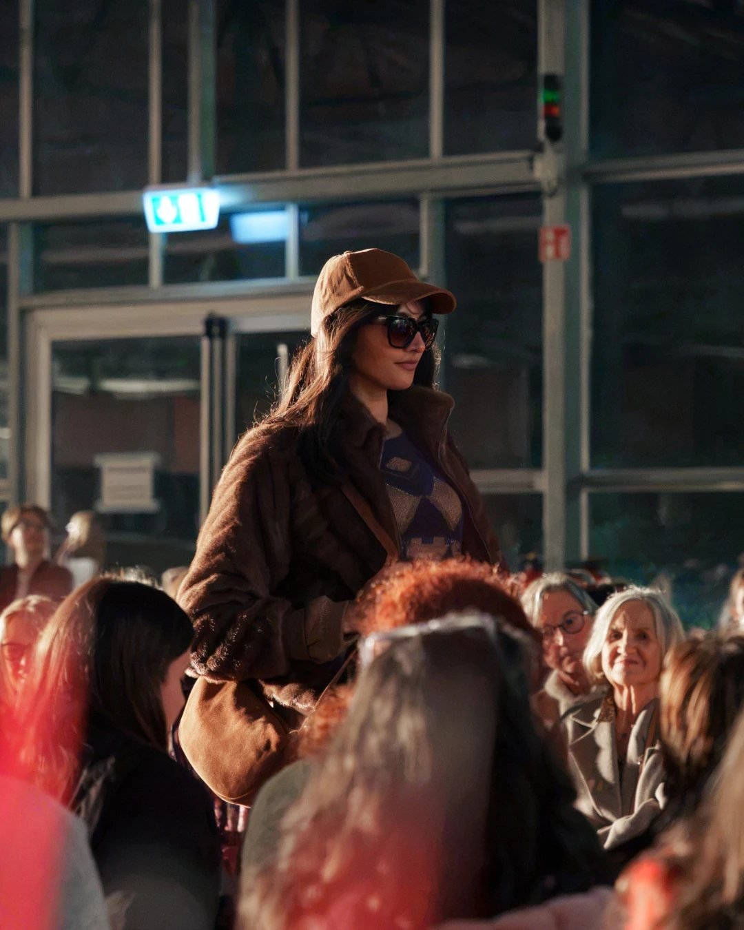 Model mit brauner Cap und Felljacke auf dem Laufsteg in der Gärtnerei